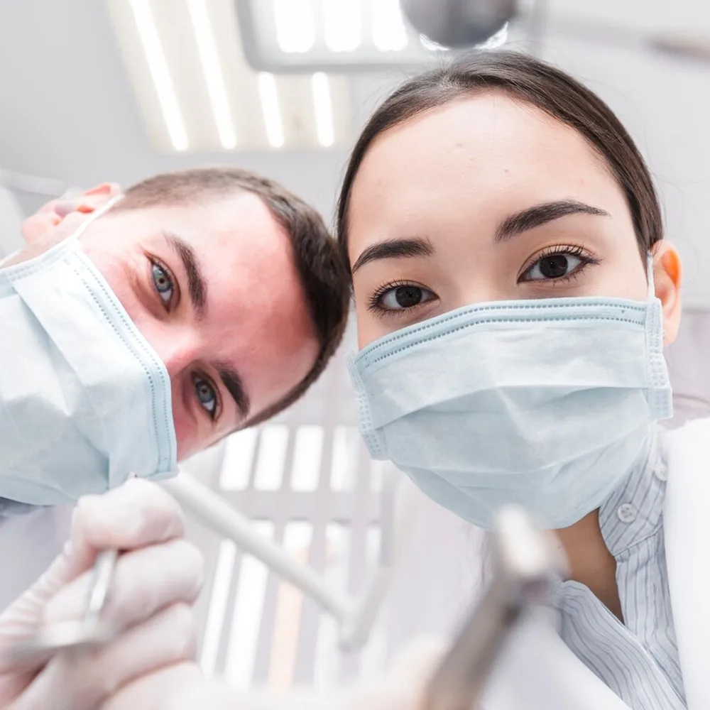 Dentist and assistant in face masks looking down at the patient